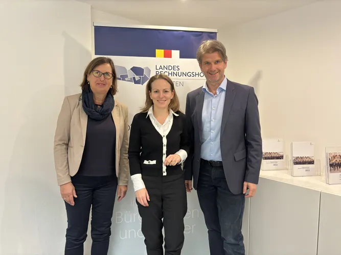 Der Landesrechnungshofdirektor, die Generaldirektorin der Bundeswettbewerbsbehörde und Prüfungsleiterin Koschat-Hetzendorf vom Landesrechnungshof stehen vor einem Roll-up des Landesrechnungshofs.